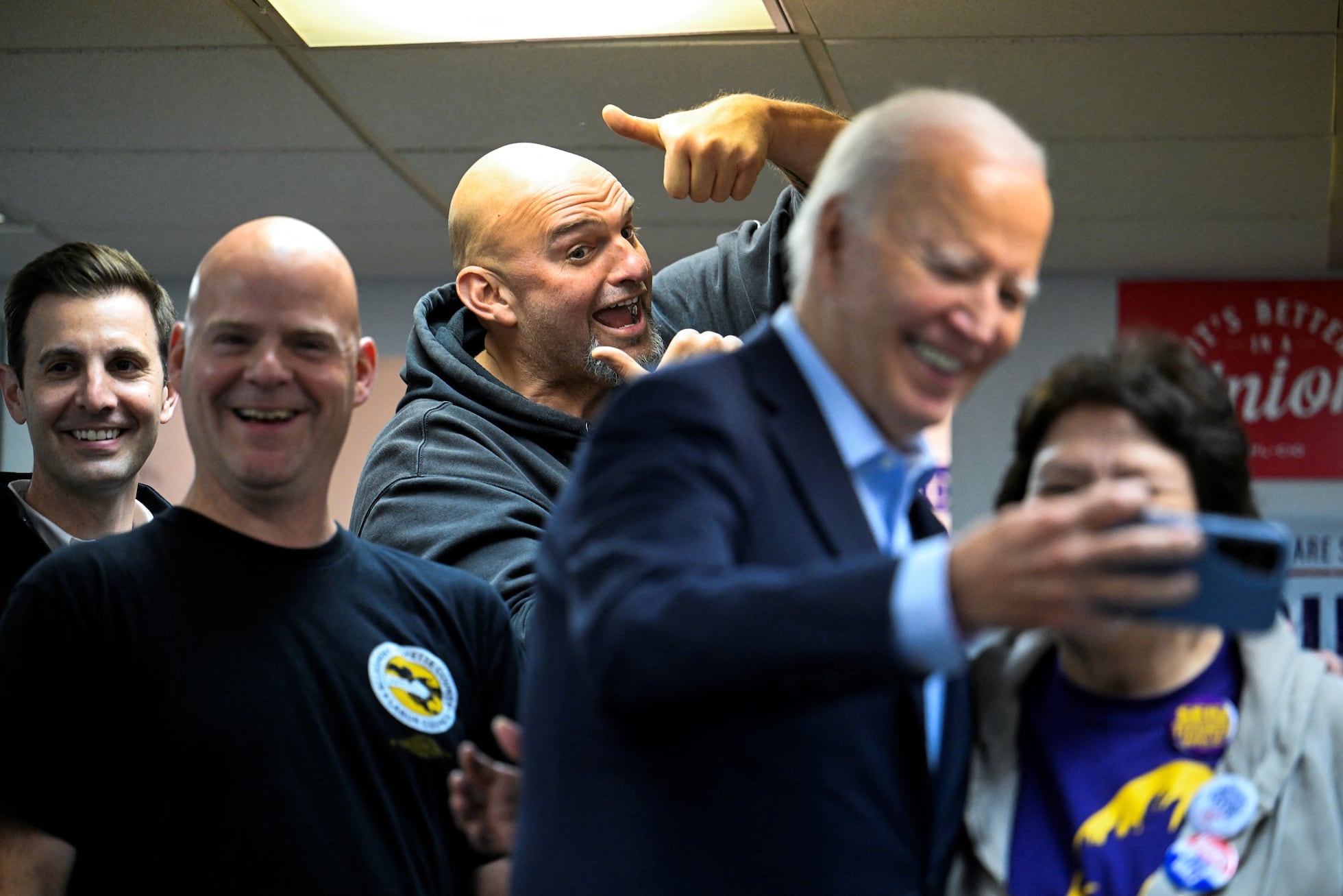 Joe Biden se hace un selfie con simpatizantes en Pittsburgh mientras el senador demócrata John Fetterman, al fondo, levanta los pulgares.