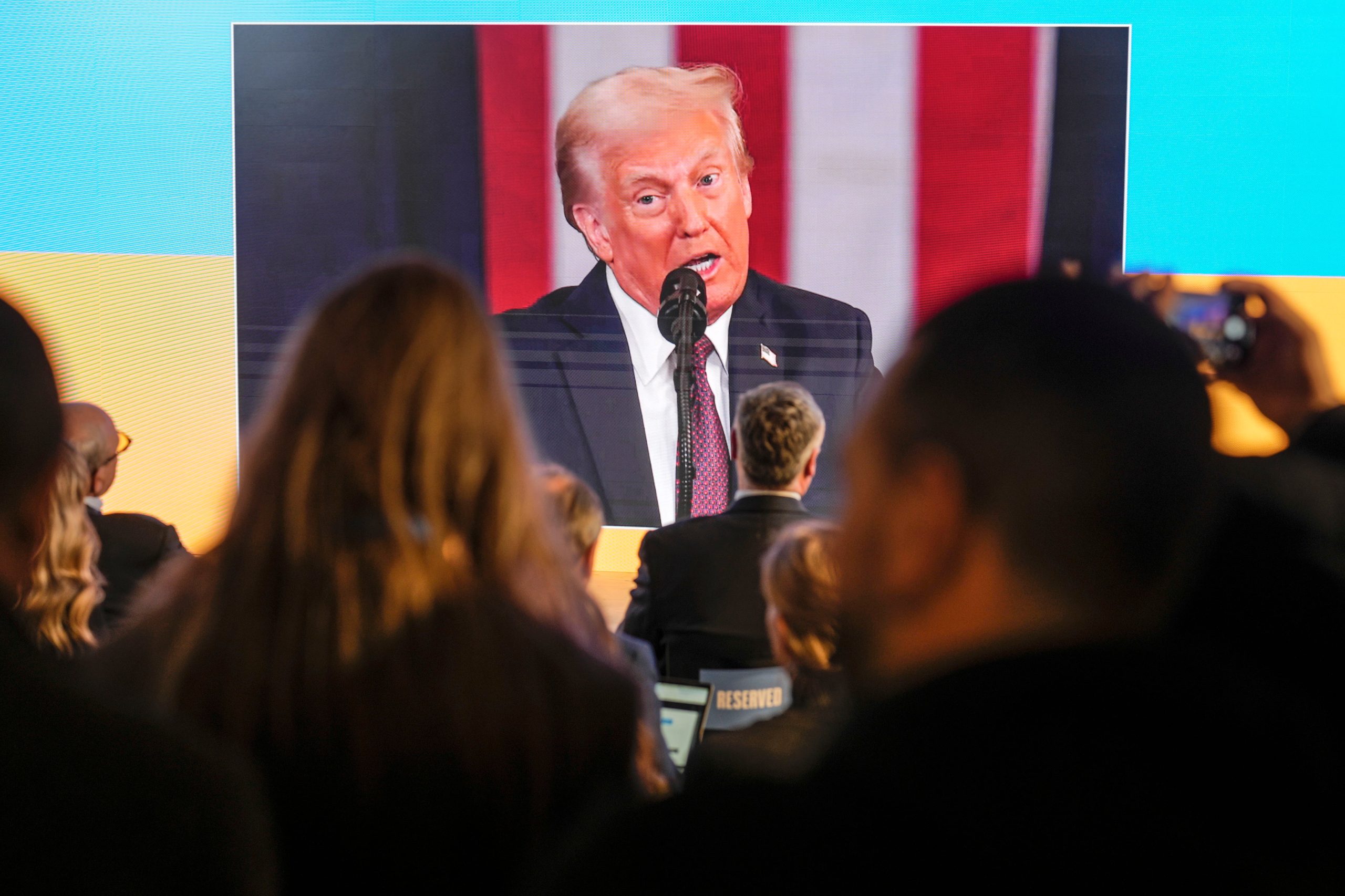 Varias personas siguen la toma de posesión de Donald Trump en pantallas en la casa de Ucrania, en el Foro Económico Mundial, en Davos, Suiza, el 20 de enero de 2025. (AP Foto/Markus Schreiber)