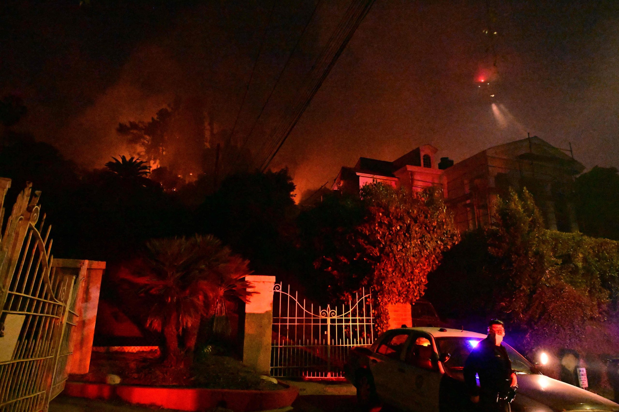 Un oficial de policía se encuentra debajo de la maleza en llamas en el Sunset Fire cerca de Hollywood Blvd en las colinas de Hollywood en Los Ángeles, California, el 8 de enero de 2025. Al menos cinco personas han muerto en los incendios forestales que arrasan Los Ángeles, según informaron las autoridades el 8 de enero. Los bomberos se han visto desbordados por la velocidad y la ferocidad de las llamas, incluso en Hollywood. (Foto de Robyn Beck / AFP)