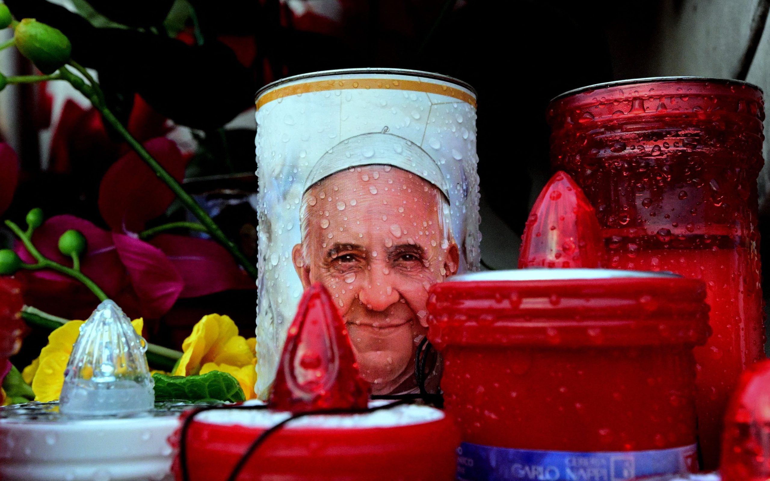 Velas que representan al Papa Francisco se colocan en la estatua de Juan Pablo II fuera del hospital Gemelli donde el Papa Francisco está hospitalizado en Roma el 24 de febrero de 2025.