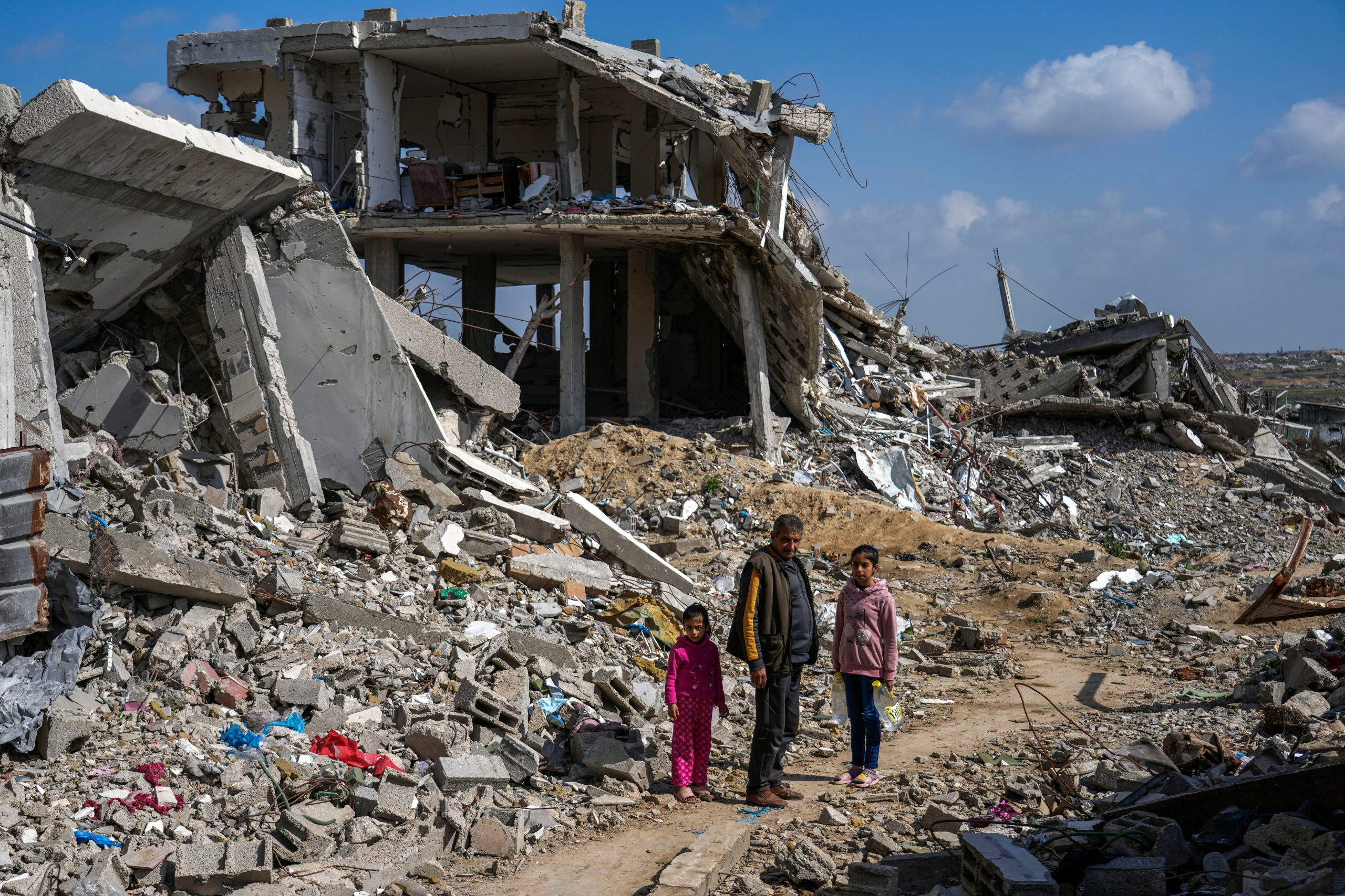 Un hombre palestino y dos niñas observan los escombros de viviendas destruidas por la ofensiva aérea y terrestre del ejército de Israel contra Hamás en el campamento para refugiados Bureij, en el centro de la Franja de Gaza, el lunes 27 de febrero de 2025