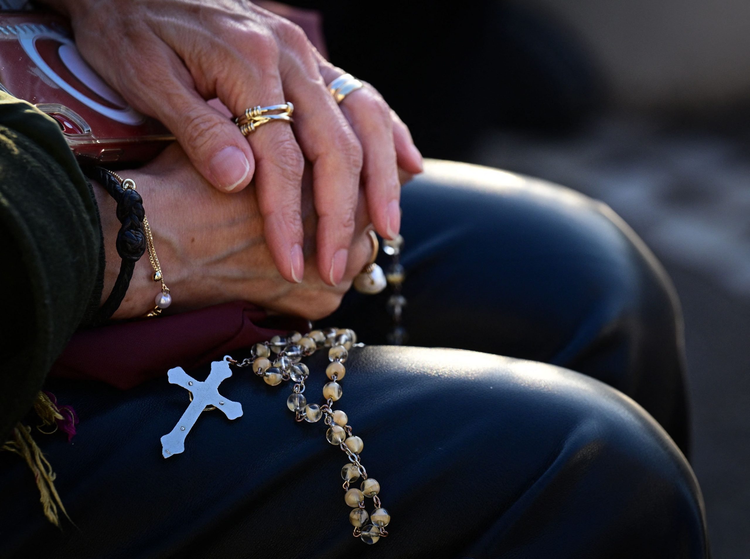 Una mujer sostiene un rosario mientras reza ante la estatua de Juan Pablo II en el exterior del Hospital Universitario Gemelli, donde el Papa Francisco está hospitalizado 