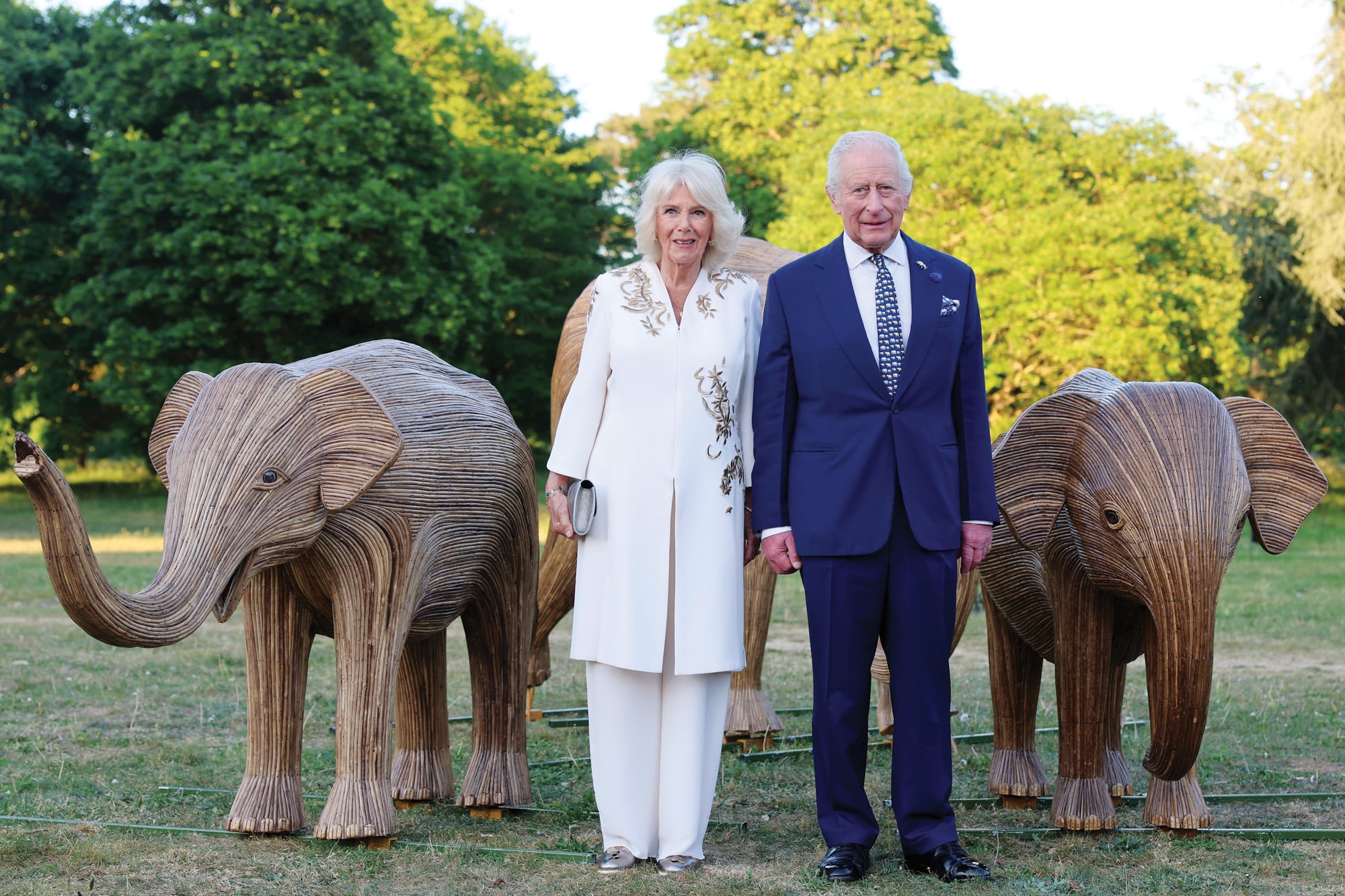 En la gala “Maravillas de la naturaleza”, los reyes posaron con nuevas obras de madera. Para la ocasión, Camilla eligió un look de la India, túnica blanca de largo midi con detalles en dorado, que combinó con un pantalón de seda haciendo juego. Carlos III optó por un traje azul, que completó con una corbata con estampa de elefantes y un broche en forma del paquidermo.