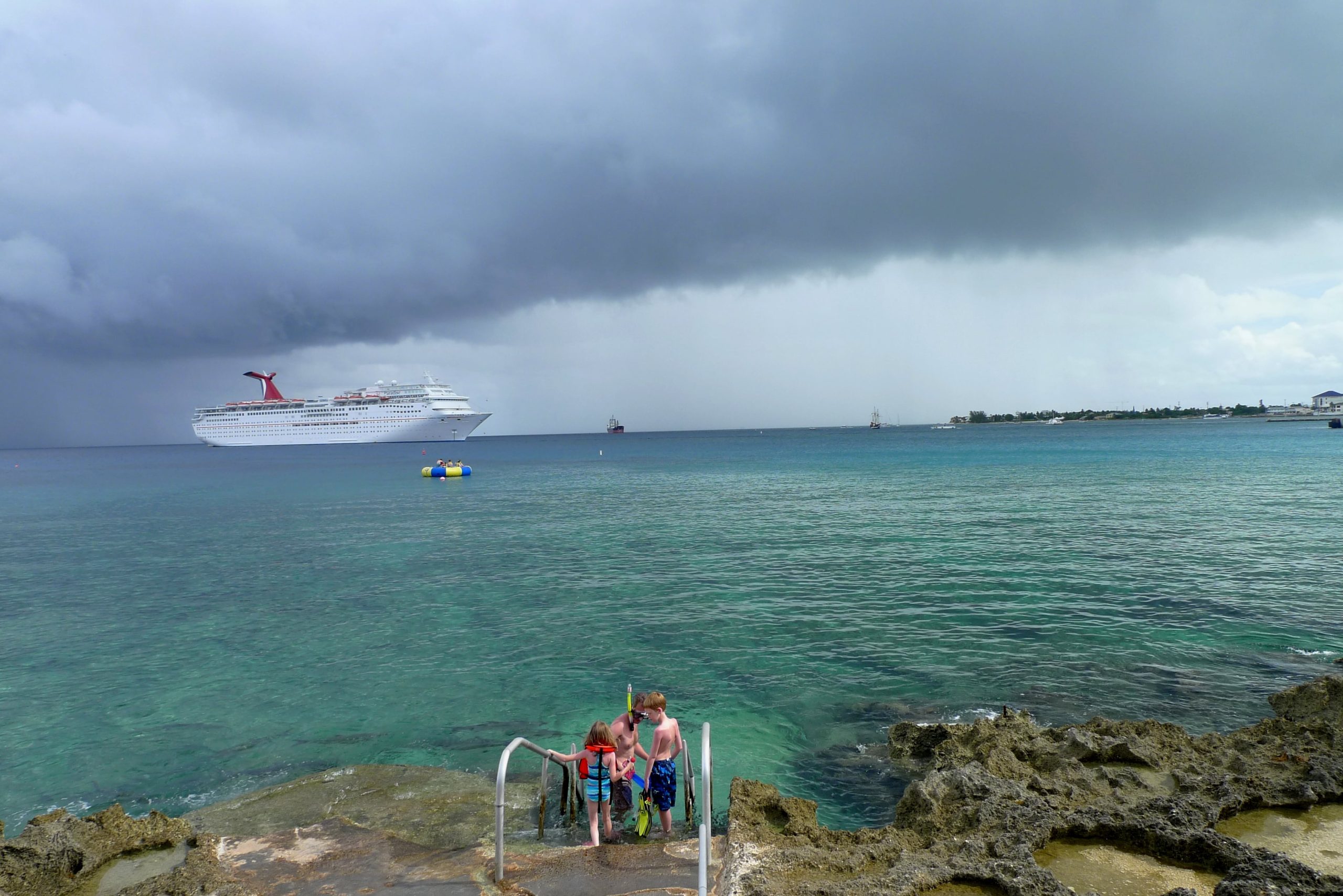 Una familia a punto de hacer snorkel, con un crucero en el horizonte.
