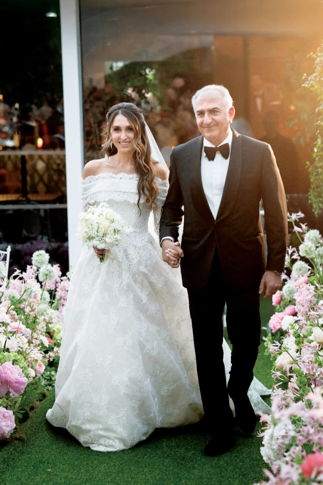 Iman llega al altar tomada de la mano de su padre, el príncipe Reza Pahlavi, hijo del Sha de Persia. La princesa lució un vestido del diseñador libanés Elie Saab de encaje y tul bordado al que le sumó un bolero que cubría sus brazos y que se quitó luego para la fiesta.