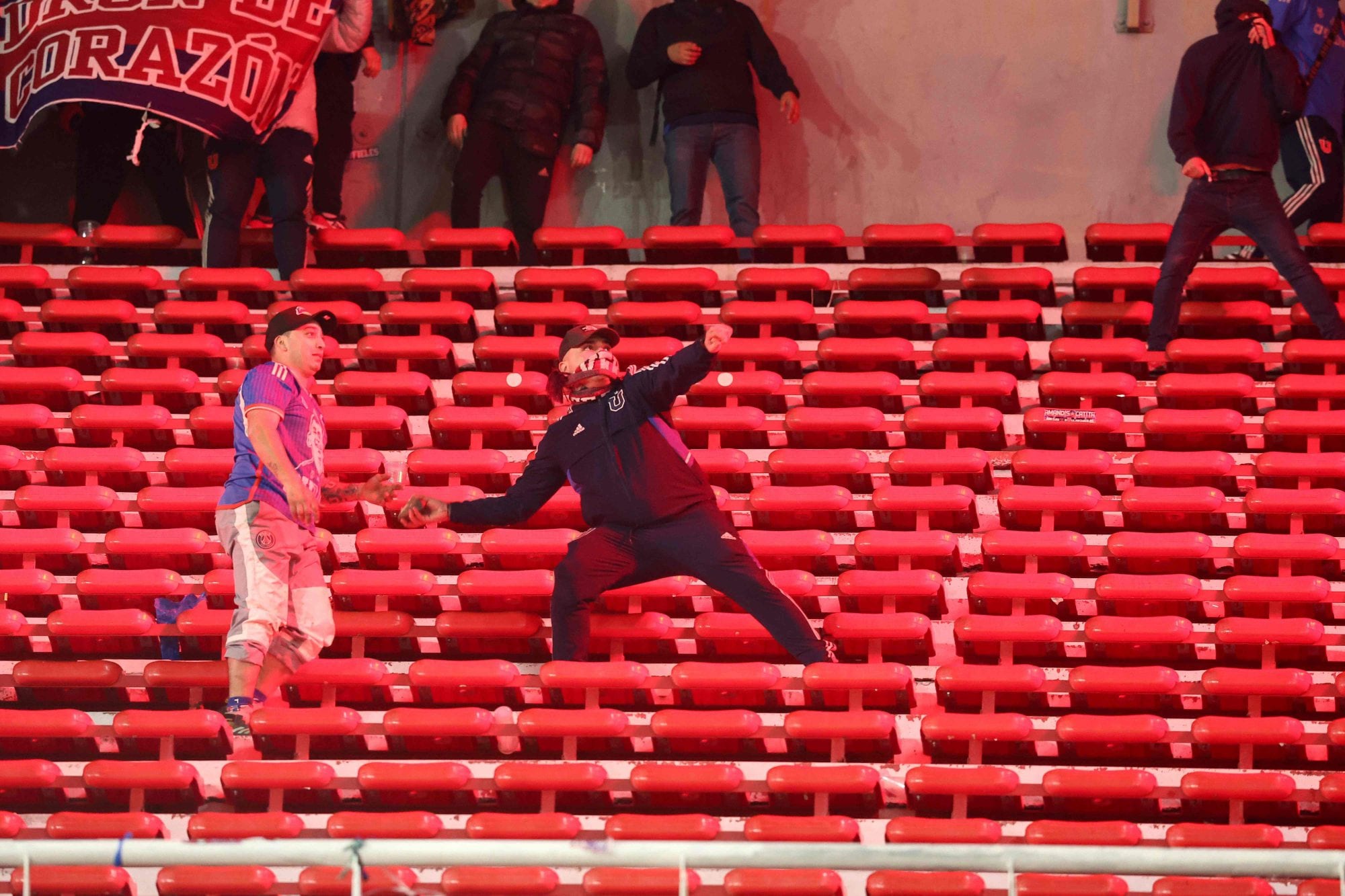 Un hincha de Universidad de Chile lanza una piedra desde el sector alto; si bien la mayoría del público visitante se marchó después de la orden oficial, varios permanecieron en la tribuna atacando a hinchas locales.