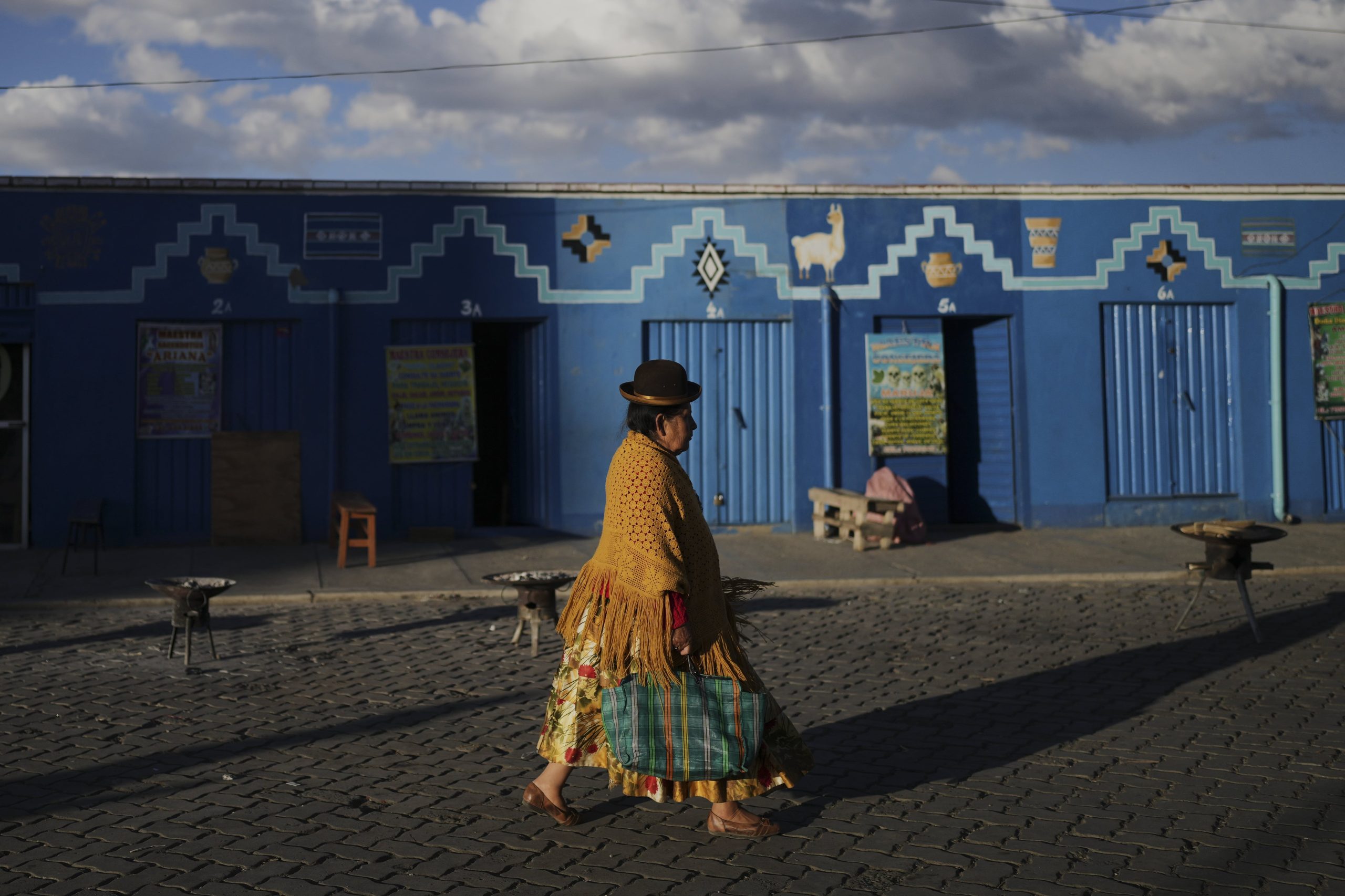 Una mujer pasa frente a los lugares de trabajo de guías espirituales aymaras en El Alto, Bolivia, el viernes 15 de agosto de 2025.