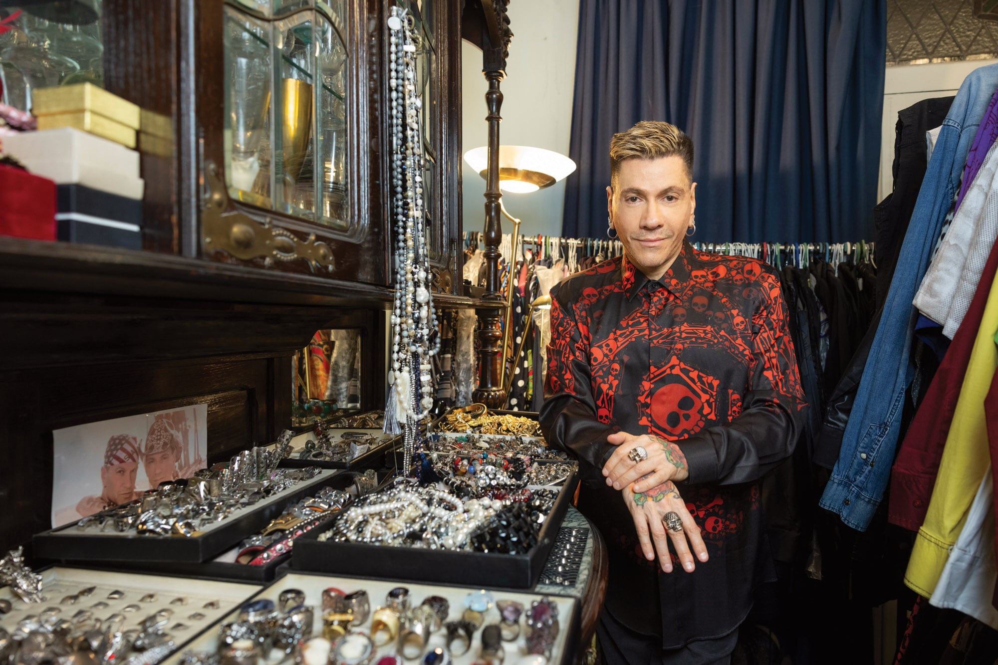 El diseñador con sus tesoros. En sus manos  muestra los anillos de calavera que combinan con la estampa de su camisa. 