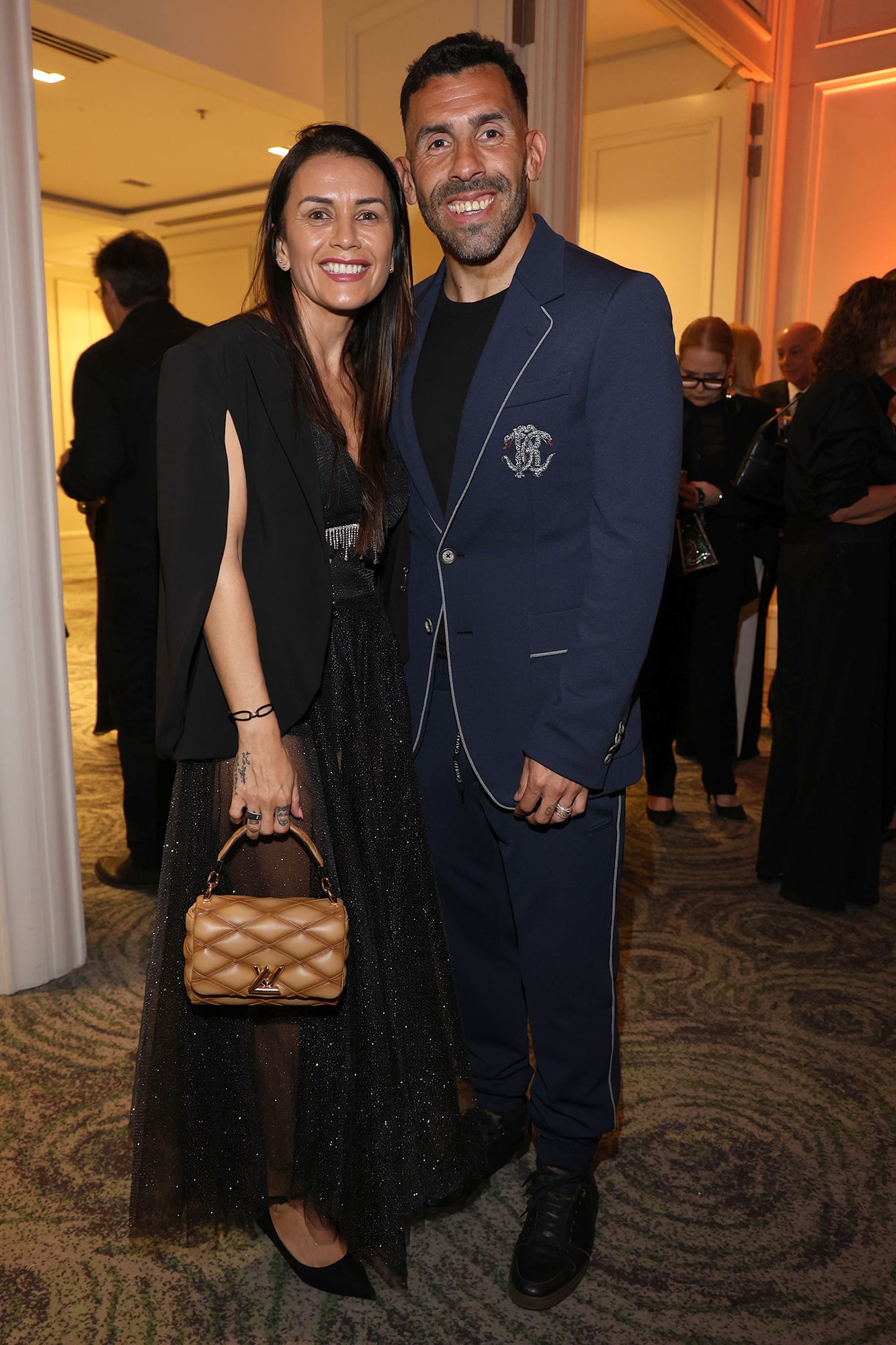 Carlos Tévez y su mujer, Vanesa Mansilla, con un transparencias, blazer-capa y una cartera de Louis Vuitton. Comprometido con la causa, el DT viajó especialmente desde Córdoba, donde dirige a Talleres, para estar en la gala 