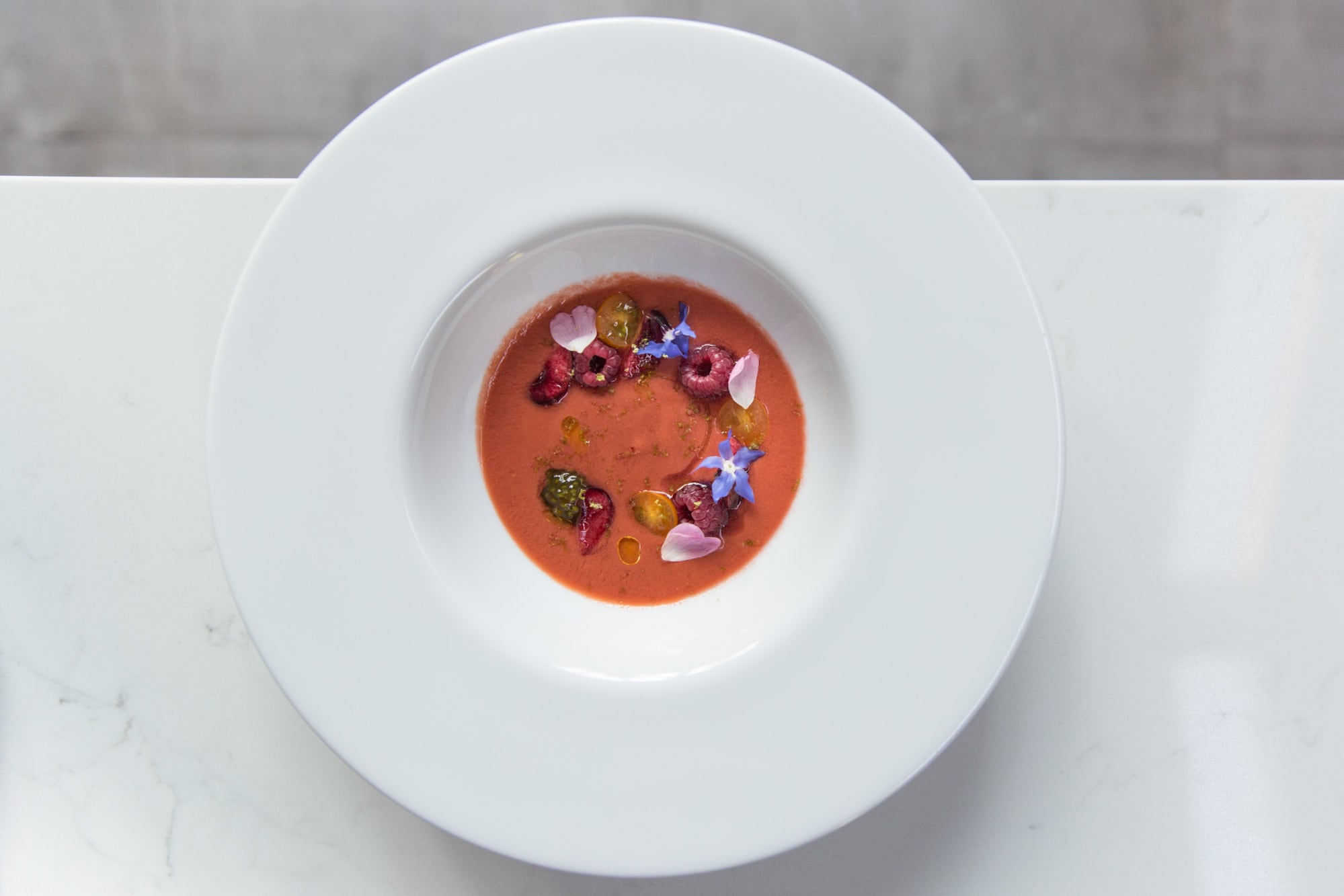 Gazpacho de tomates y cerezas negras, frambuesas y flores comestibles en Quetro.