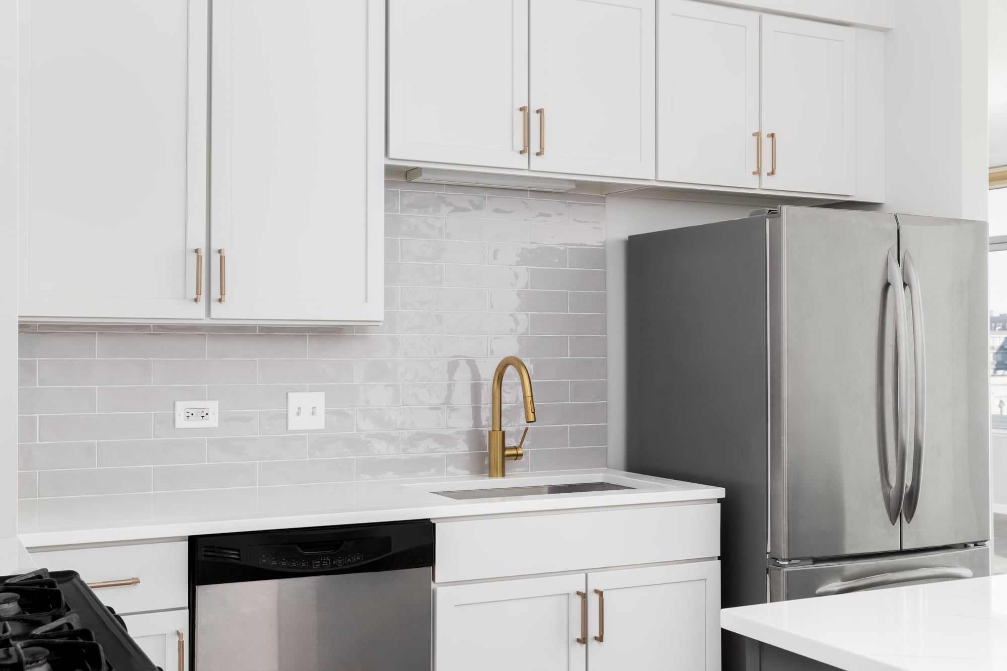 Una cocina clásica con alacenas blancas, grifería y herrajes dorados, backsplash de azulejos y mesadas de cuarzo blanco