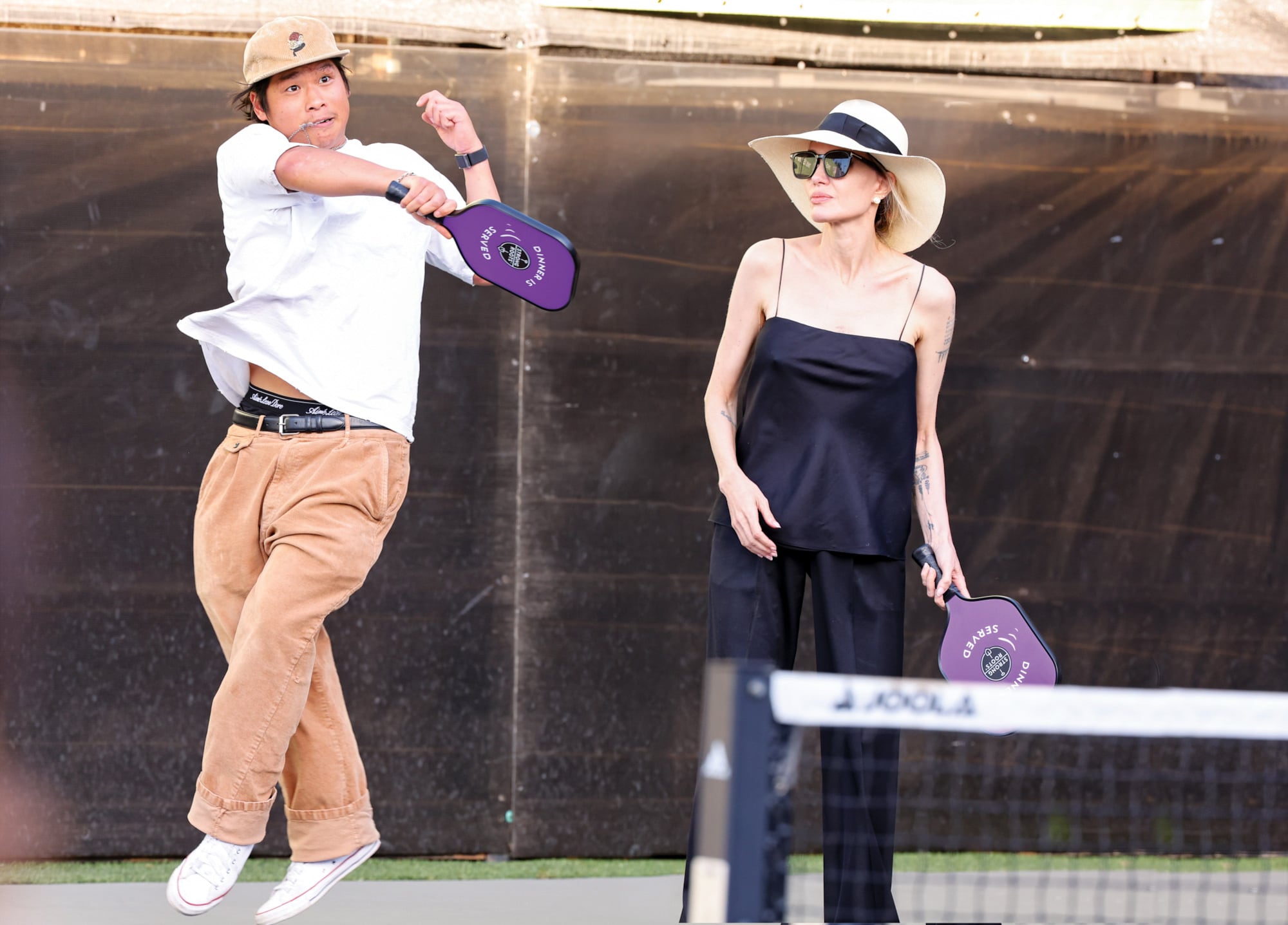 Con paletas iguales en la mano, Angelina Jolie y Pax Thien Jolie-Pitt jugaron un partido de dobles. En la imagen, Pax salta para devolver la pelota mientras su madre, de sombrero de ala, lo observa orgullosa