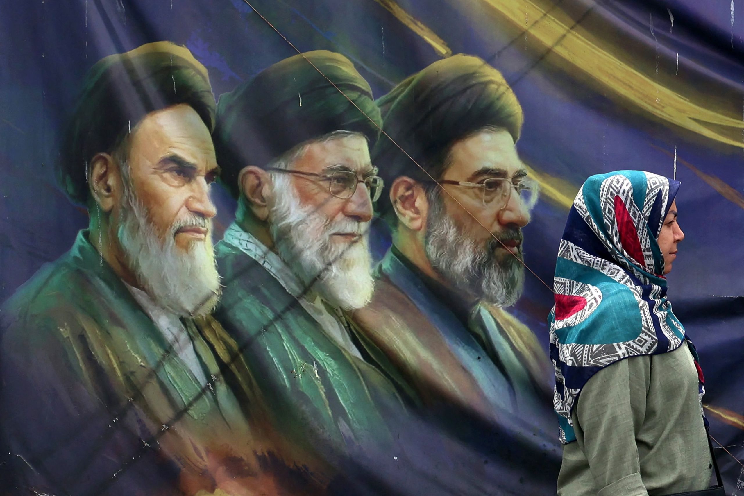 Una iraní pasa junto a un cartel con retratos del difunto fundador de la República Islámica, el ayatollah Ruhollah Khomeini, el ayatollah Ali Khamenei, asesinado el 28 de febrero pasado, y el actual líder supremo Mojtaba Khamenei, en Teherán