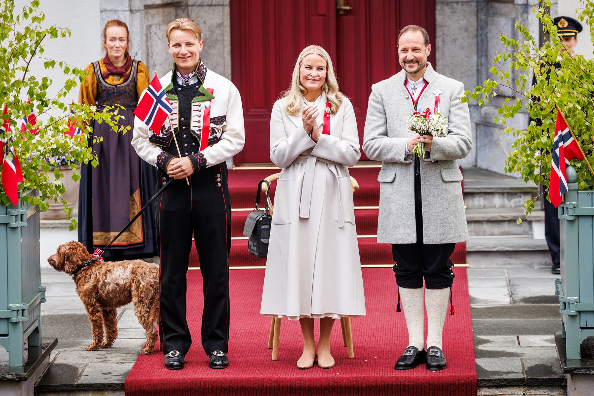 La princesa heredera, en su última aparición pública, el 17 de mayo, durante el Día de la Constitución de Noruega, en Oslo. A la izquierda,  el príncipe Sverre Magnus -con el perro de la familia-; y, a la derecha, su marido, Haakon, el príncipe heredero al trono. Durante un tramo de la celebración, Mette-Marit tuvo que sentarse en una banqueta