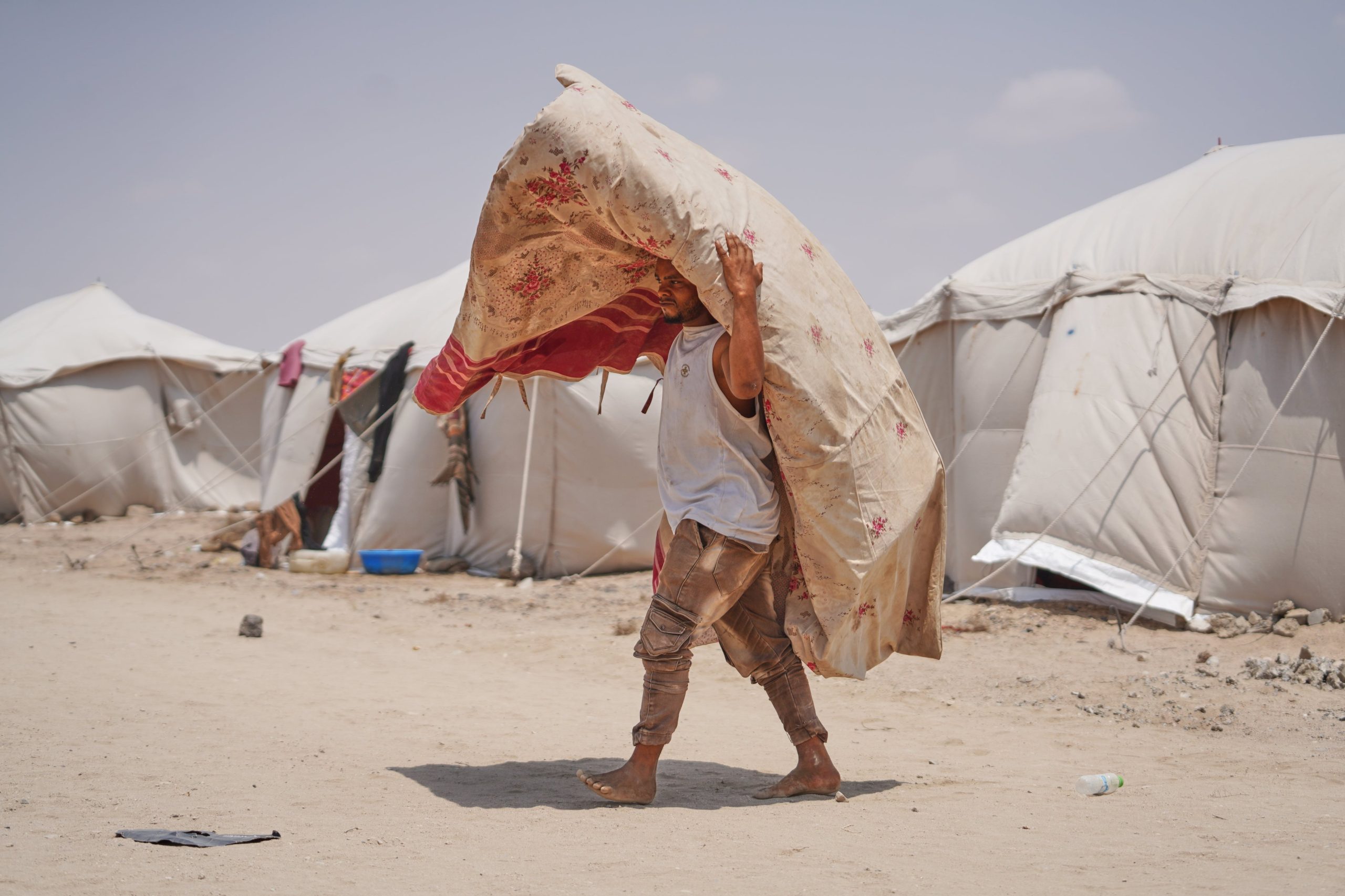 Un desplazado yemenita transporta una alfombra en el campamento Al-Firdaws, en Ras Imran, a las afueras de Adén, Yemen