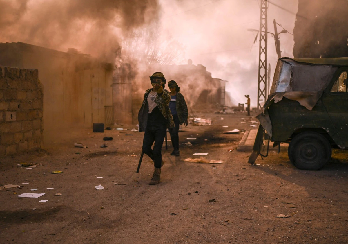 Unos hombres caminan entre columnas de humo después de que la gente saqueara e incendiara el complejo de viviendas militares de Najha, en el sureste de Damasco