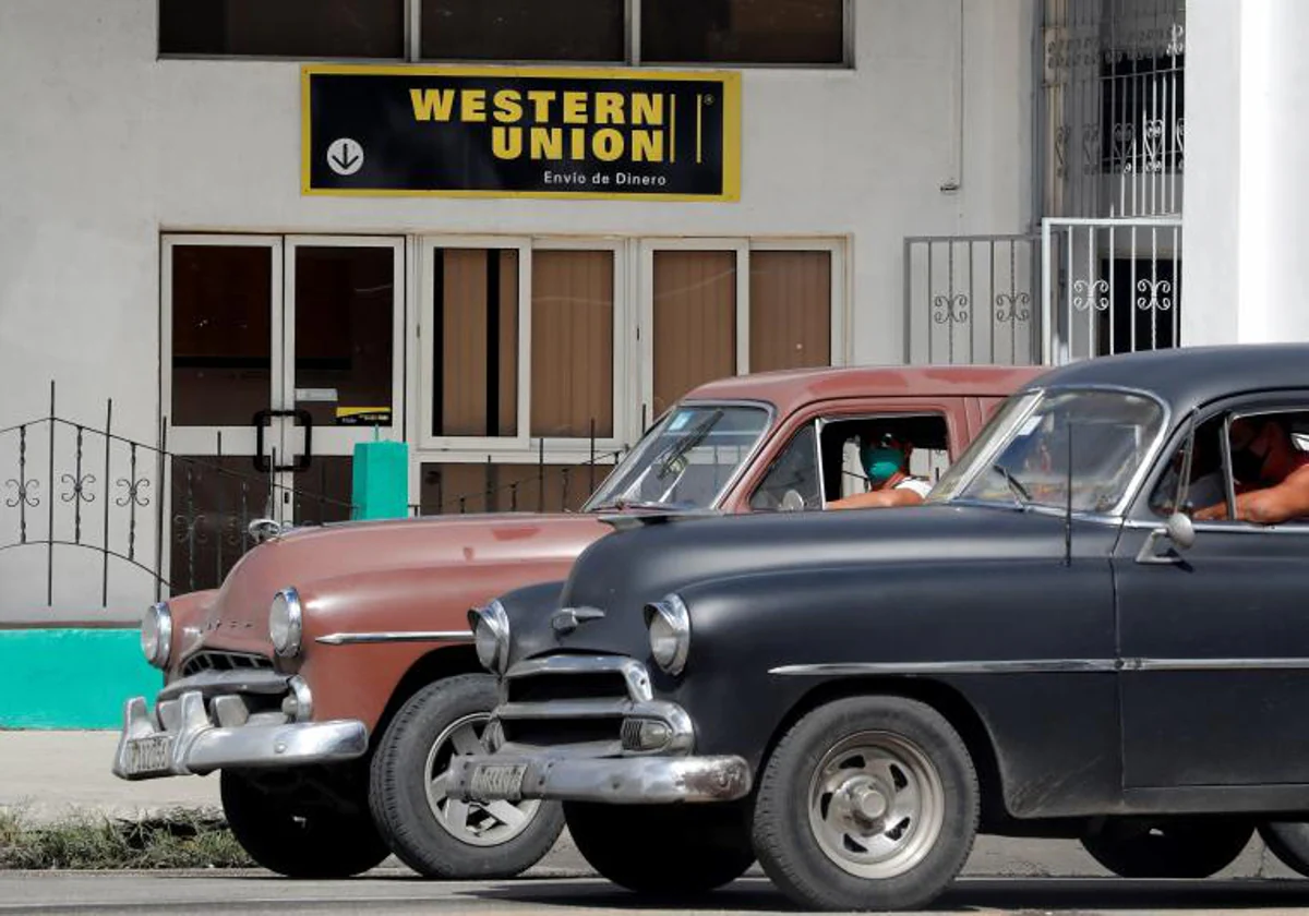 Dos autos clásicos pasan frente a una oficina de remesas, en La Habana