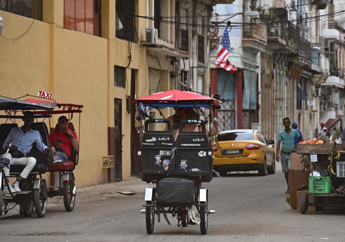 Un bicitaxi decorado con una bandera estadounidense circulando por una calle de La Habana