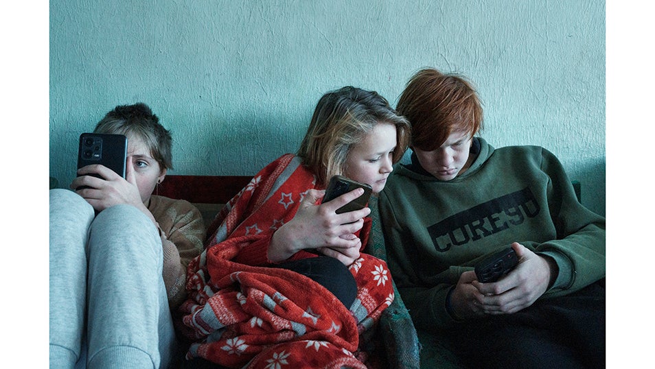 Yulia, Oleksandra y Danylo, tres niños desplazados de Lysychansk, se refugian en la luz de sus teléfonos móviles mientras permanecen en un albergue para desplazados en Zolochiv