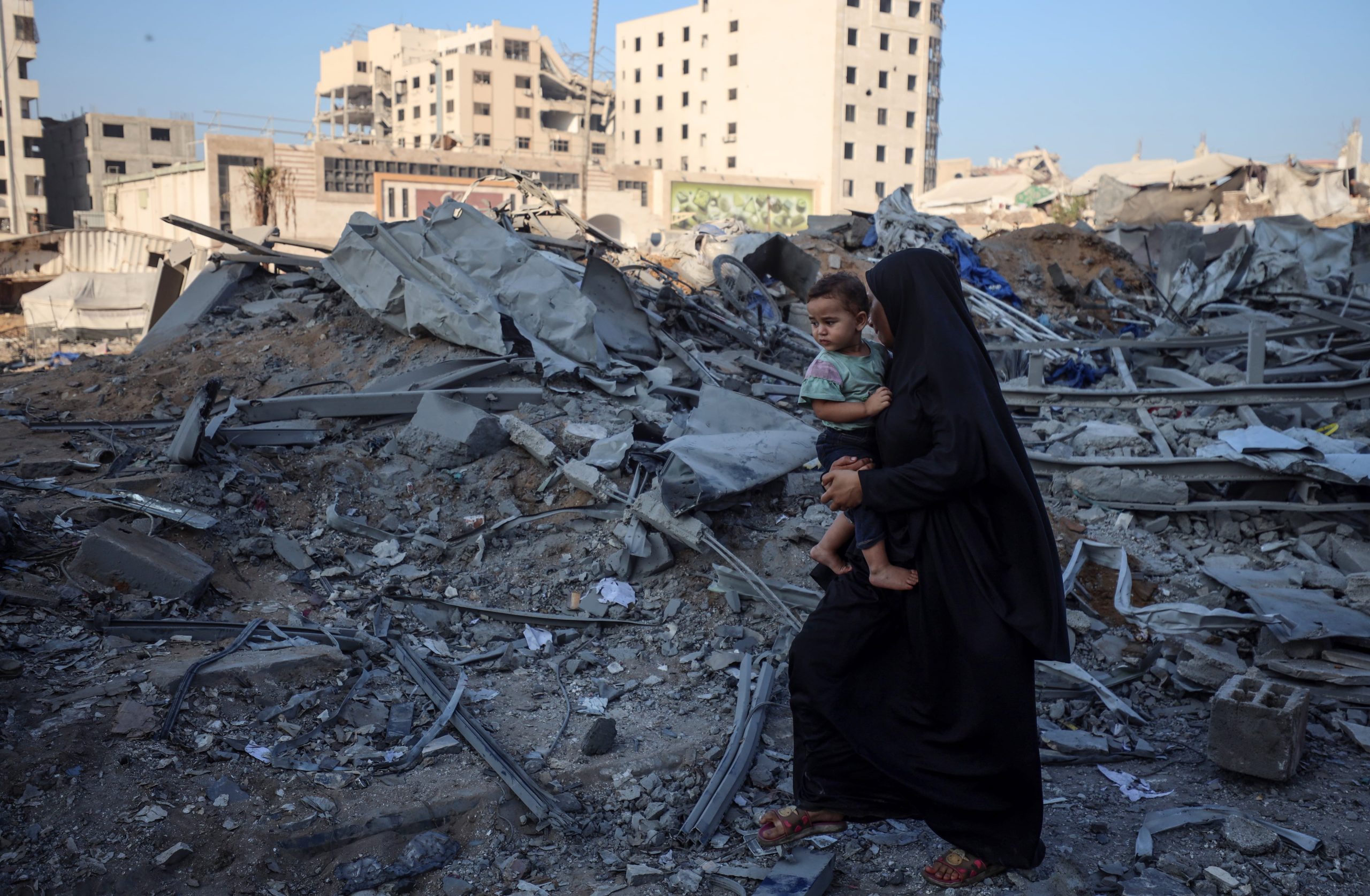 Una mujer camina con un niño en brazos por las ruinas de Ciudad de Gaza.