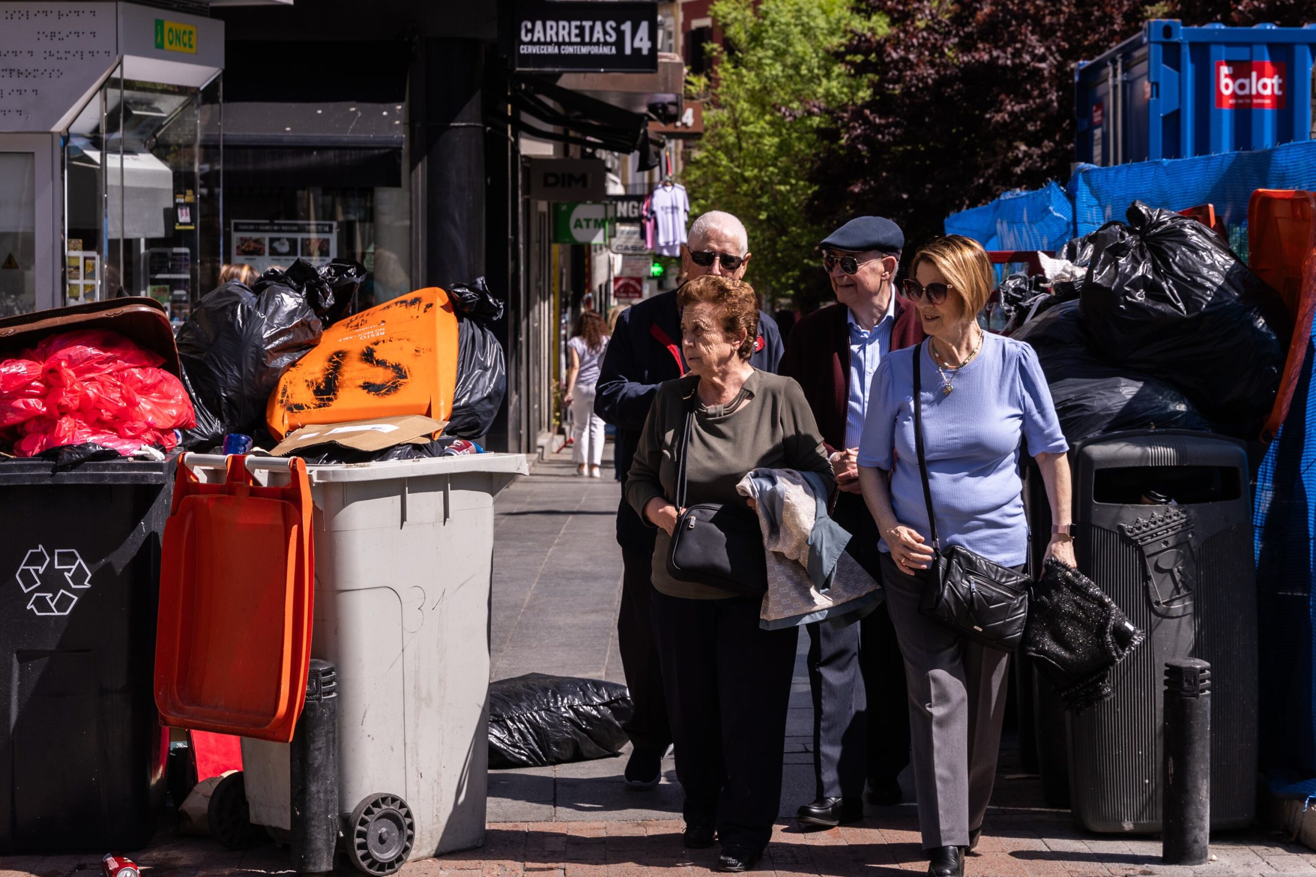 Cuatro personas pasan junto a varios cubos en el centro de Madrid en plena huelga de basuras en abril de 2025. 