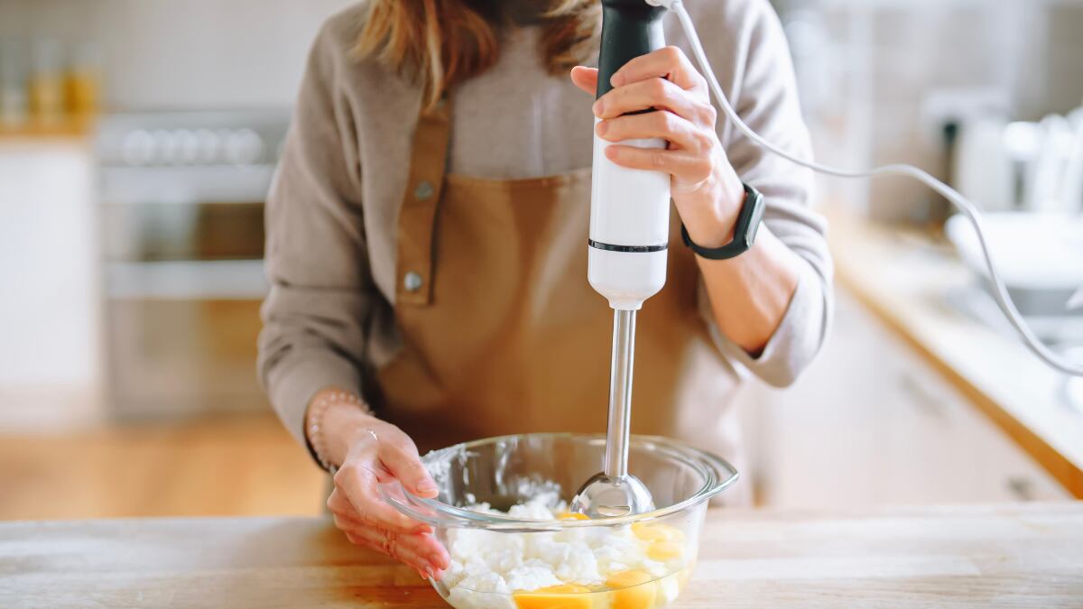 Mujer usando una batidora de mano para preparar una mezcla cremosa.