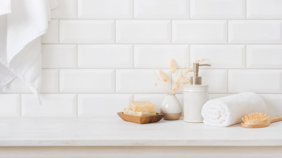 Accesorios de higiene en mesa de madera en baño sobre pared de azulejos.
