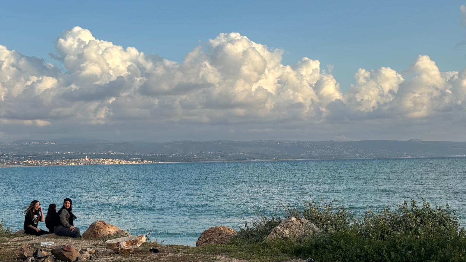 Tres chicas observan el horizonte desde la costa de Tiro mientras una humareda se levanta a lo lejos en los territorios fronterizos, el lunes.