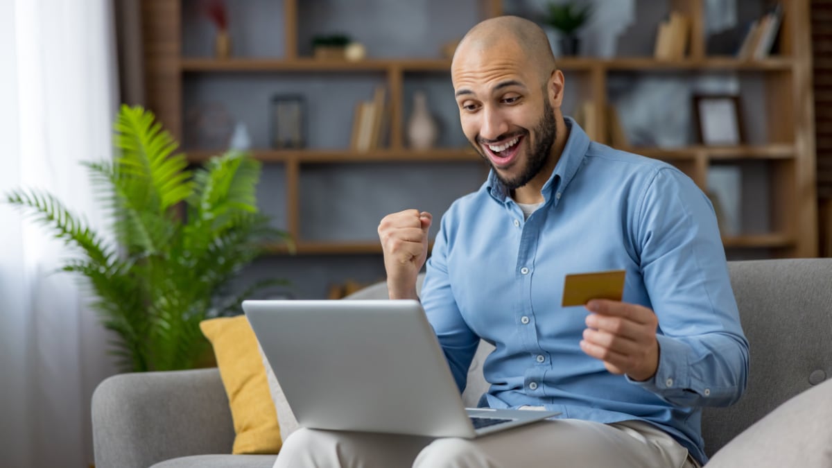 Hombre sonriente completando con éxito un pago en línea con tarjeta de crédito.
