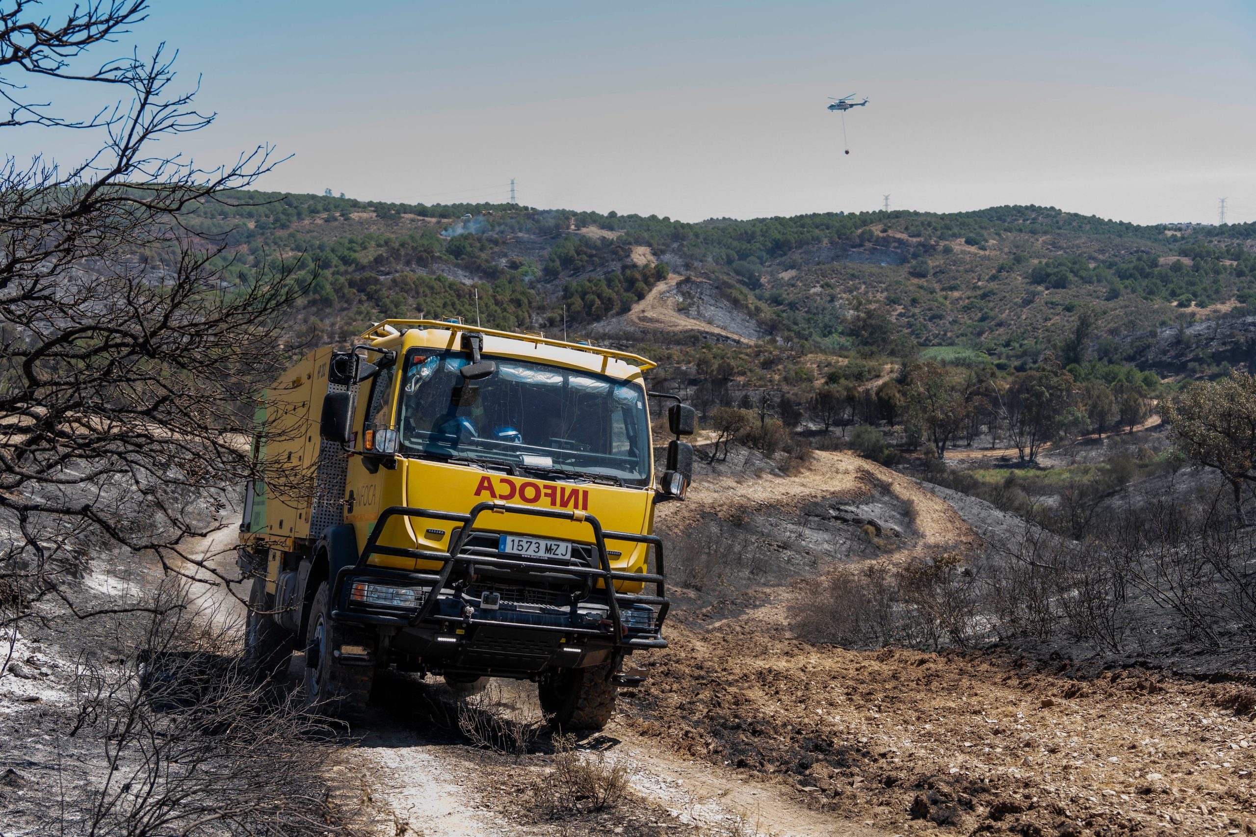 Un camión y un helicóptero del INFOCA en las inmediaciones del incendio declarado este lunes en el paraje de Los Turbios, en el término municipal de Villanueva de los Castillejos (Huelva)