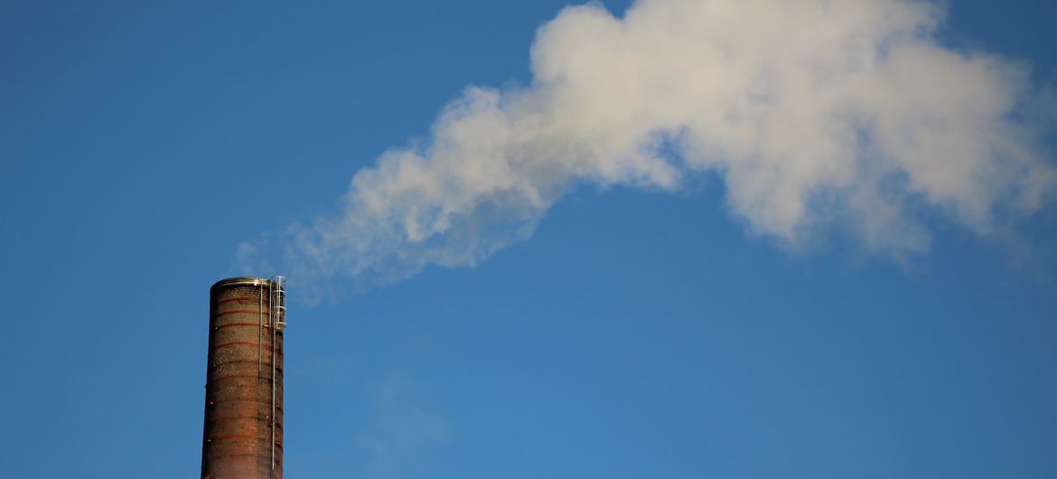 Una chimenea industrial emite una gran columna de humo blanco contra un cielo azul despejado.
