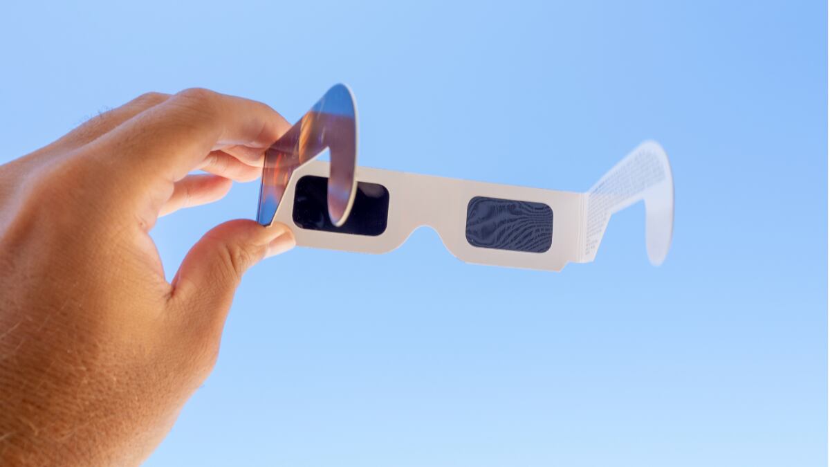 Una mano sosteniendo unas gafas para ver el eclipse solar.