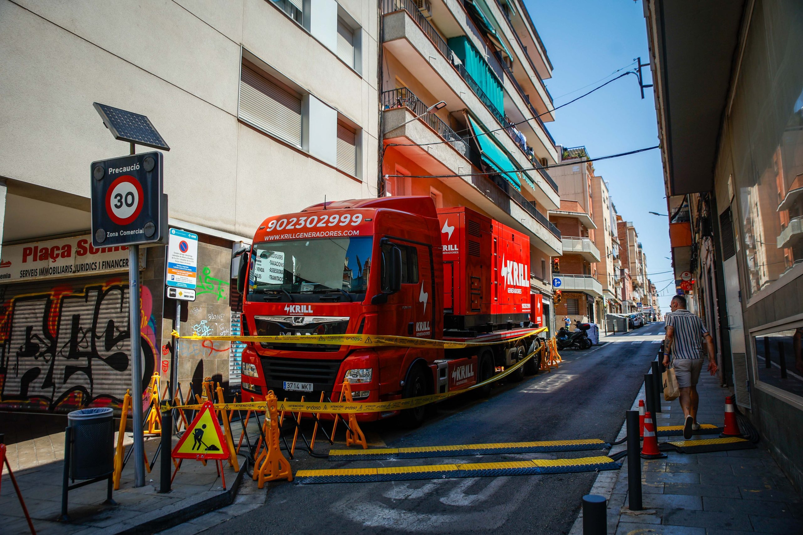 Una persona pasa junto a uno de los generadores eléctricos que están suministrando luz a los barrios afectados por el incendio en la subestación eléctrica de Collblanc.