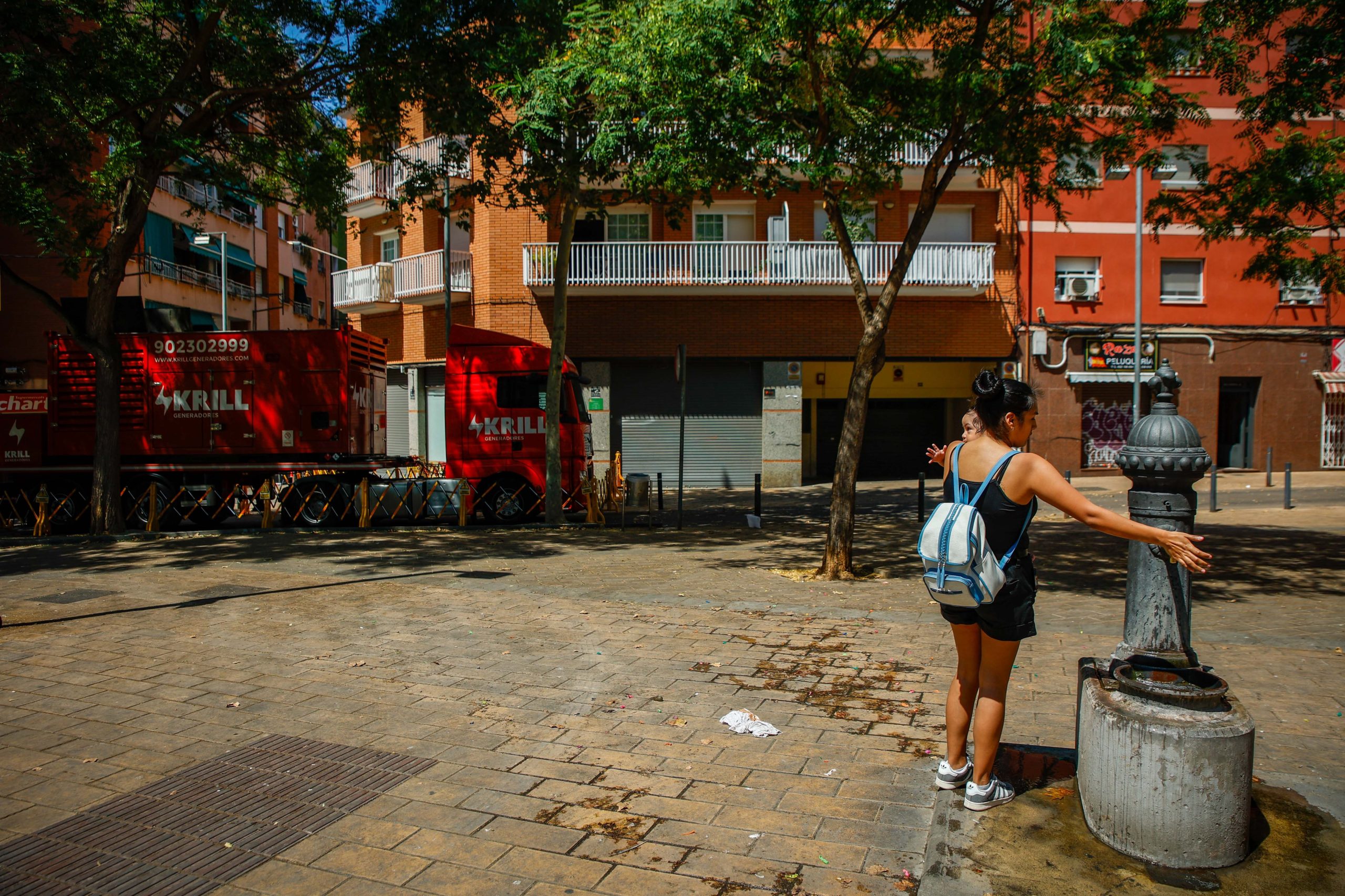 Una mujer moja la cabeza de su hija en una fuente pública delante de unos de los generadores instalados para dar servicio de luz-