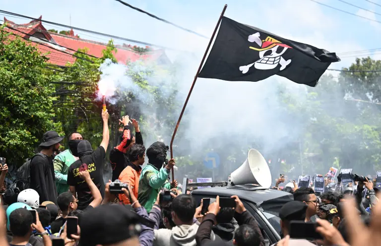 Manifestantes sostienen una bengala y ondean una bandera pirata del anime japonés One Piece, tendencia en internet utilizada para criticar las políticas gubernamentales.